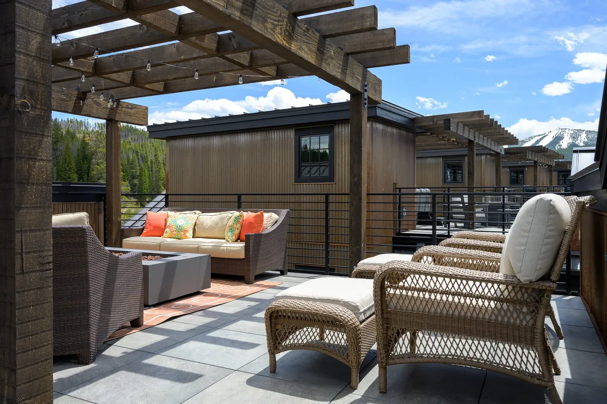 A wooden pergola shades a plush outdoor seating area, complete with decorative cushions and surrounded by lush greenery. The setting is serene and ideal for morning relaxation or evening entertaining.