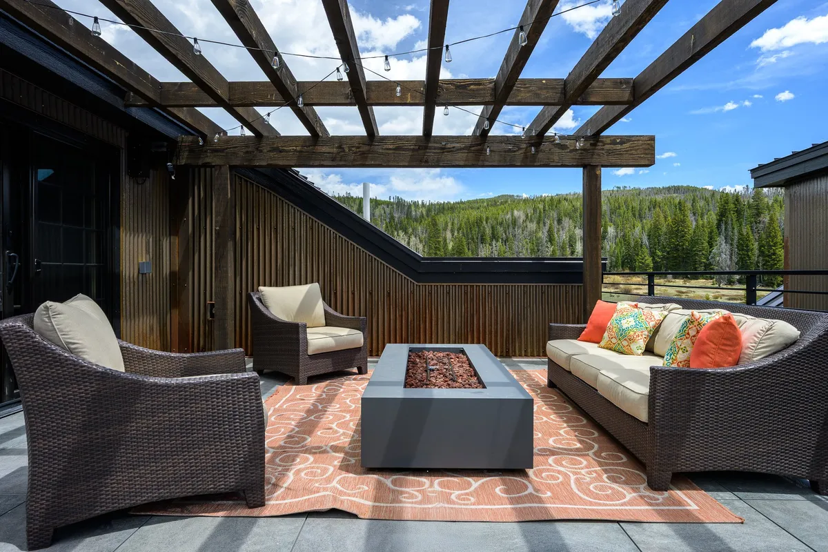 The hero image showcases the villa's inviting patio space, featuring a modern pergola, a cozy fire pit surrounded by plush outdoor seating, all set against breathtaking mountain vistas. The scene is tranquil, with golden sunset light illuminating the outdoor area, hinting at perfect evenings for relaxing, stargazing, or gathering with friends and family.