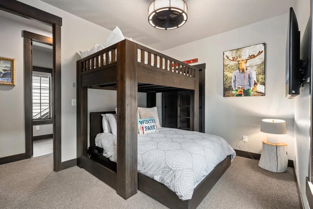 A playful bunk bedroom featuring a full-over-queen bunk bed, a decorative pillow, whimsical moose artwork, and a reading lamp. The room feels inviting, cozy, and family-friendly, perfect for children or group stays.