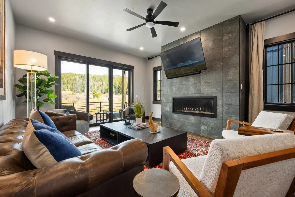 A plush living room featuring a leather sofa positioned in front of a custom fireplace, with a large window offering a scenic view and a 65" HD smart TV mounted on the wall. The space exudes comfort, with inviting seating arranged for conversations, movie nights, or relaxing after outdoor adventures.