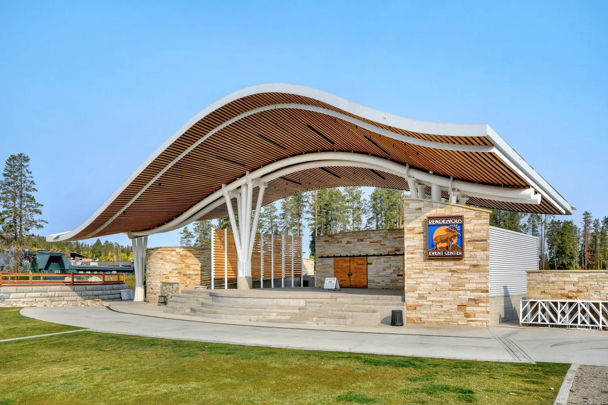 A festive exterior shot of a curved roof structure, stone facade, and steps leading up to a popular event venue. The setting is clearly designed for concerts, community gatherings, and cultural experiences.