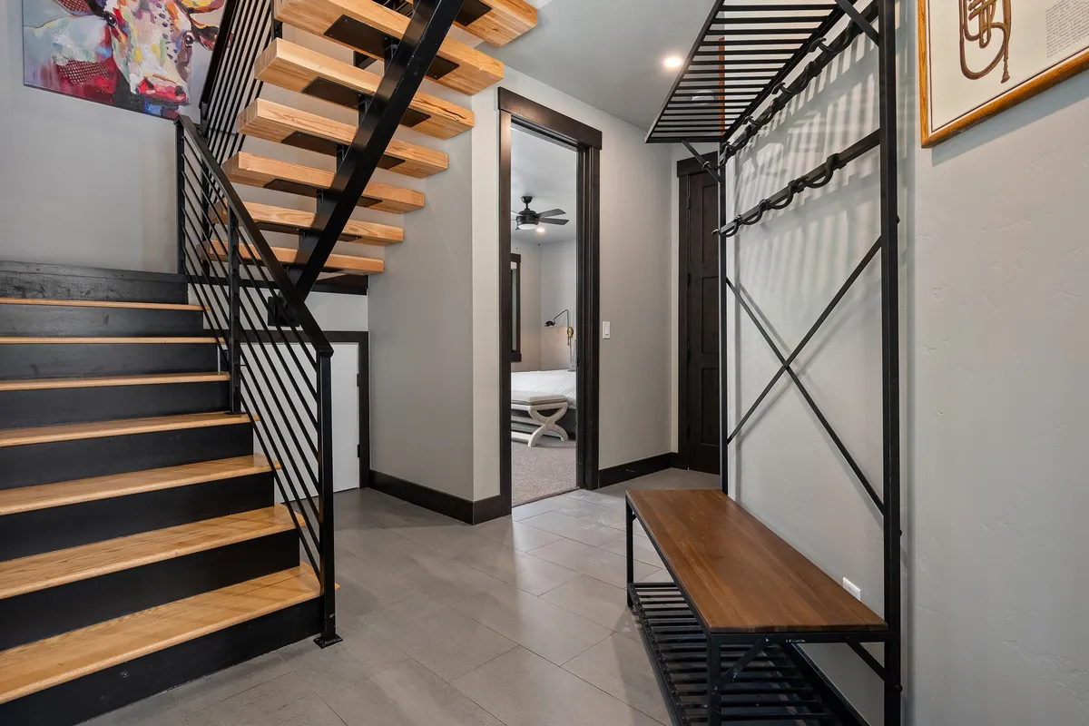 This interior shot captures a stylish entry space with a modern staircase, bench with storage for shoes or gear, and artwork on the wall—embodying a functional and attractive mudroom or entryway.
