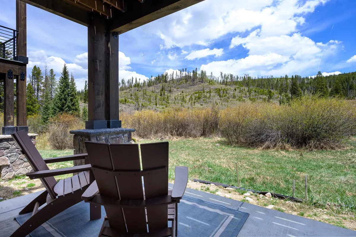 A tranquil exterior scene featuring wooden chairs set on a grassy area, looking out over a stunning mountain view under an open sky. The setting exudes peace and offers a direct connection to the natural landscape, perfect for relaxation or informal gatherings.