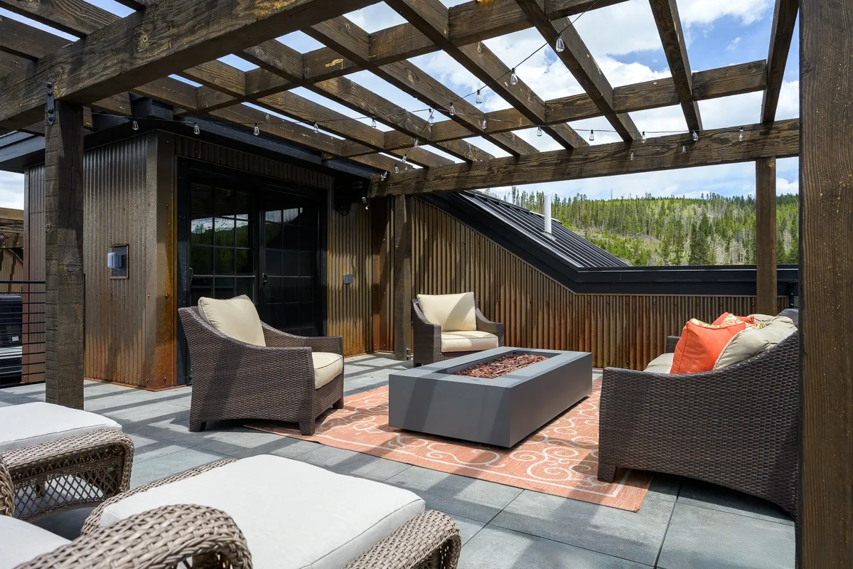 A stylish fire pit is surrounded by comfortable seating beneath a pergola, set in beautifully landscaped outdoor space. The area is designed for socializing, relaxing, and enjoying warmth on cool evenings, with the landscape creating a cozy yet open feel.