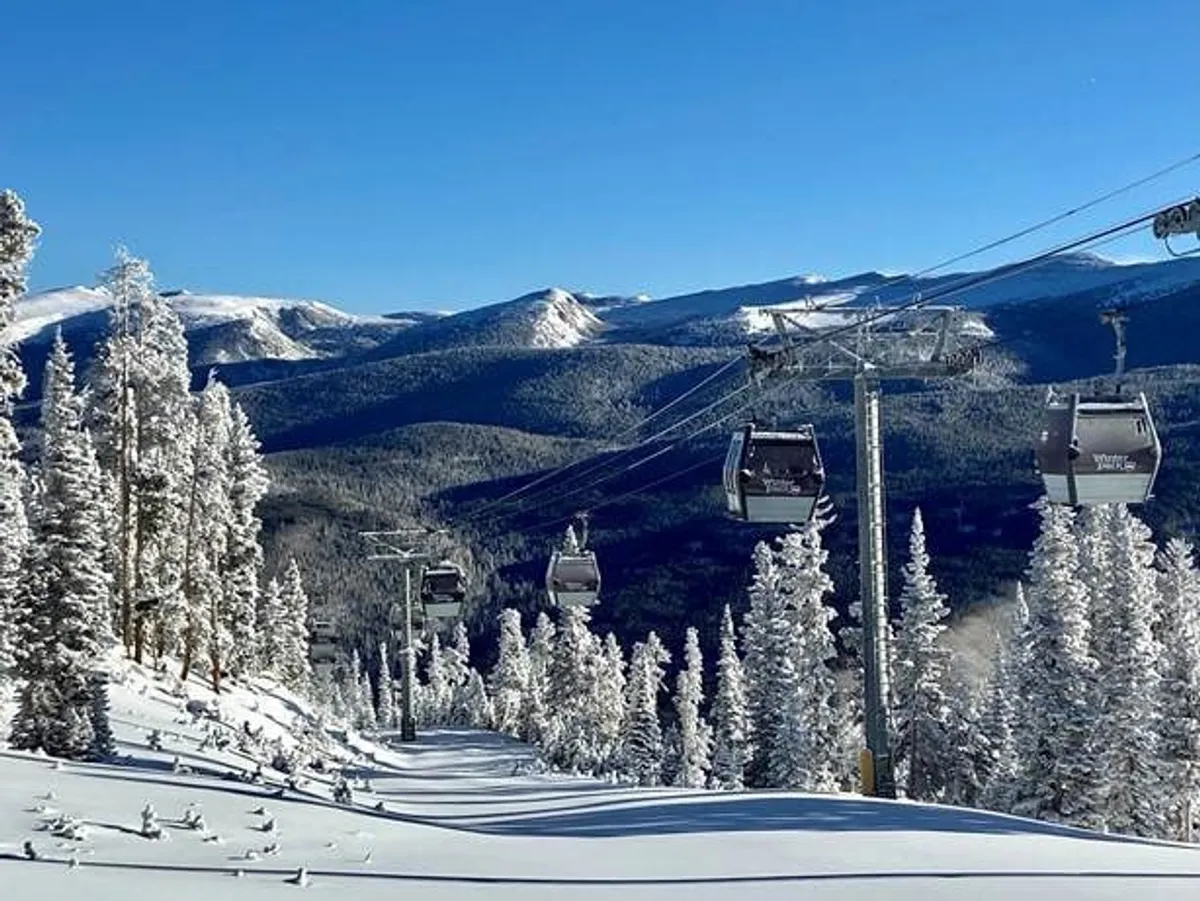 A sweeping outdoor winter scene featuring gondola lifts gliding above snow-covered trees with a majestic mountain range in the background. The crisp snow and adventure-ready lifts hint at nearby ski slopes, snowboarding, and other winter activities.